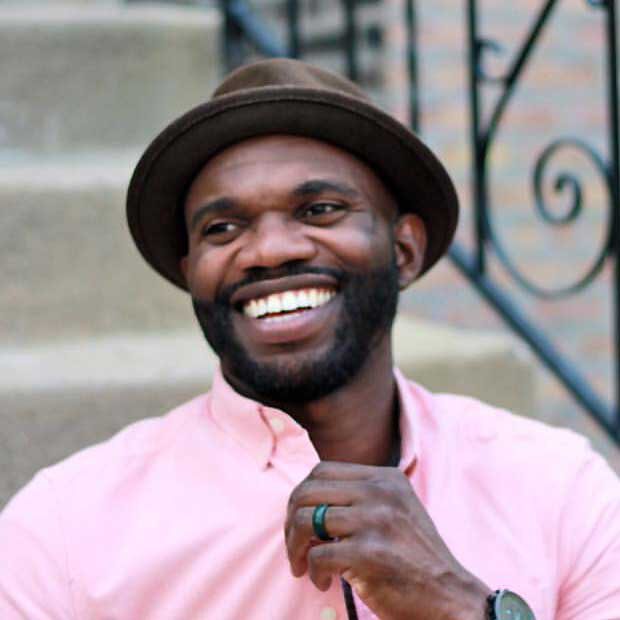 Portrait of Augie Emuwa, black male smiling with hat and pink shirt